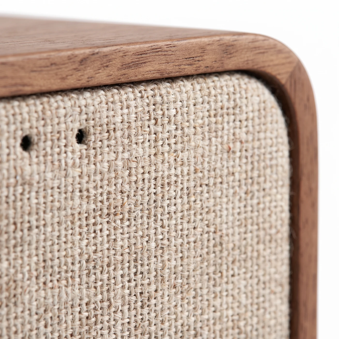 Macro of the coarse oatmeal woven speaker cloth meeting the rounded, hand-oiled walnut corner of the cabinet.